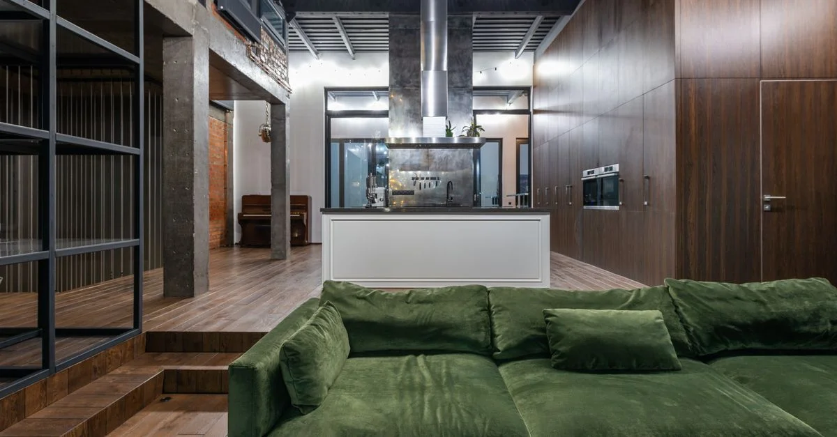Loft moderne spacieux avec un élégant canapé vert, décor industriel et cuisine épurée.