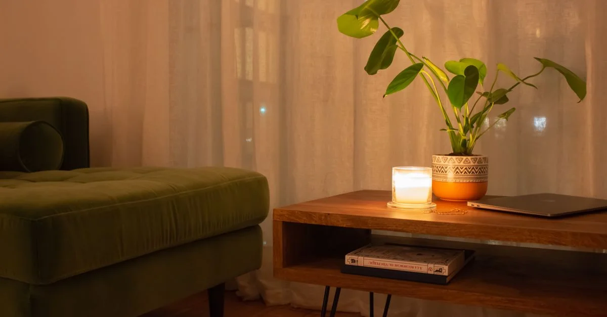 Salon chaleureux et accueillant avec une bougie, un canapé vert et une plante en pot sur une table en bois.
