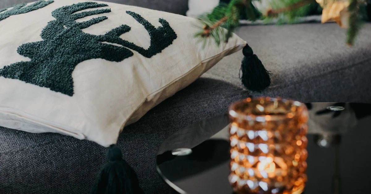 Scène de salon chaleureux avec un coussin de rennes et une bougie lumineuse.