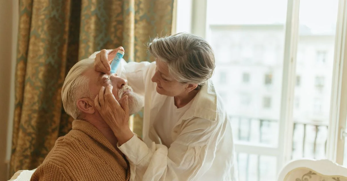Une femme senior applique des gouttes oculaires à son partenaire à la maison, montrant soin et affection.