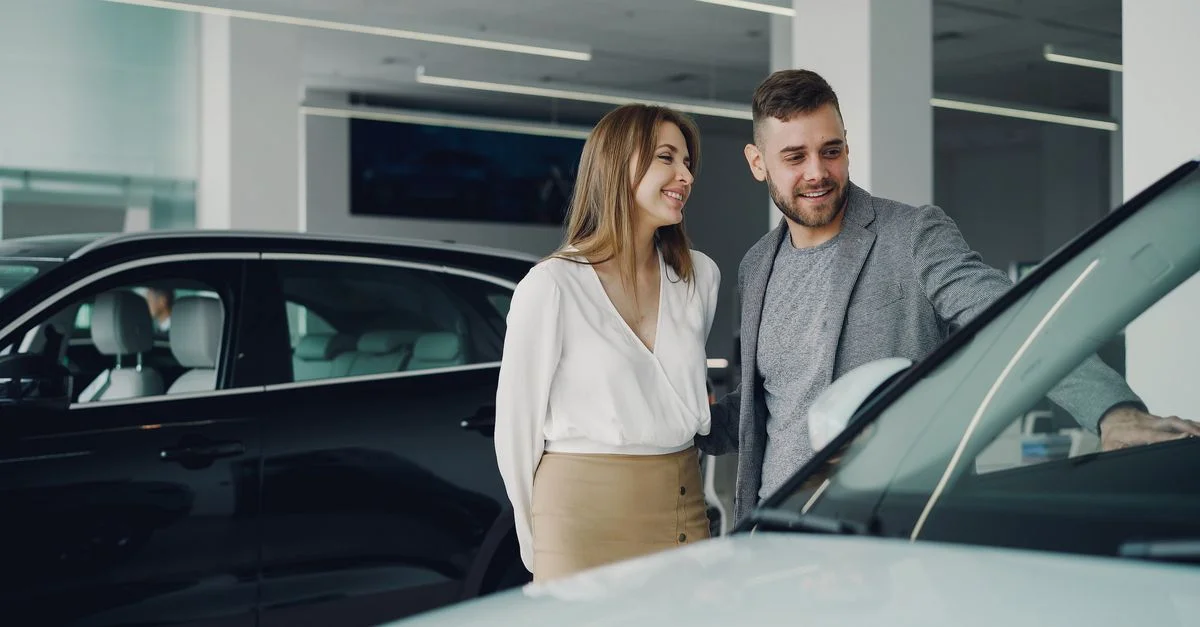Un couple souriant explore des voitures chez le concessionnaire, profitant de l'expérience d'achat.